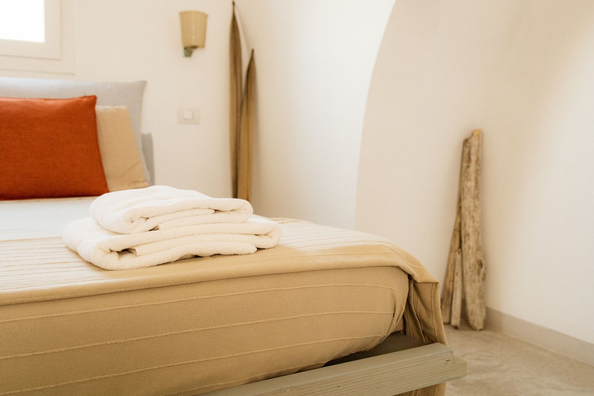 Un lit bien fait, avec un matelas et des oreillers de couleur beige, une pile de serviettes blanches et un banc en bois au pied du lit.