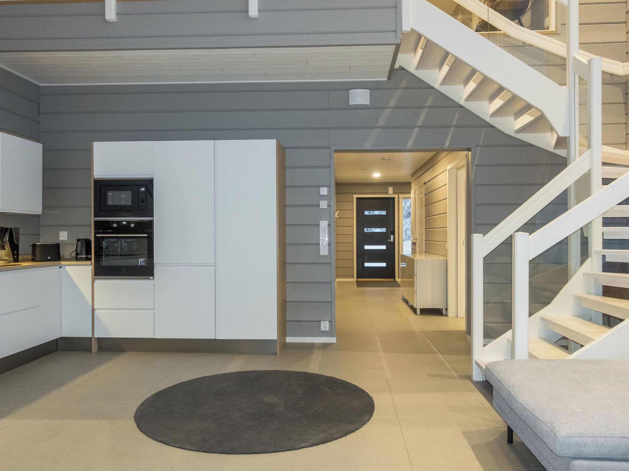 A modern kitchen with built-in appliances, a staircase, and a hallway leading to another room.