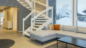 Un interior moderno con una escalera espiral blanca, un sofá seccional gris y ventanas amplias con persianas.