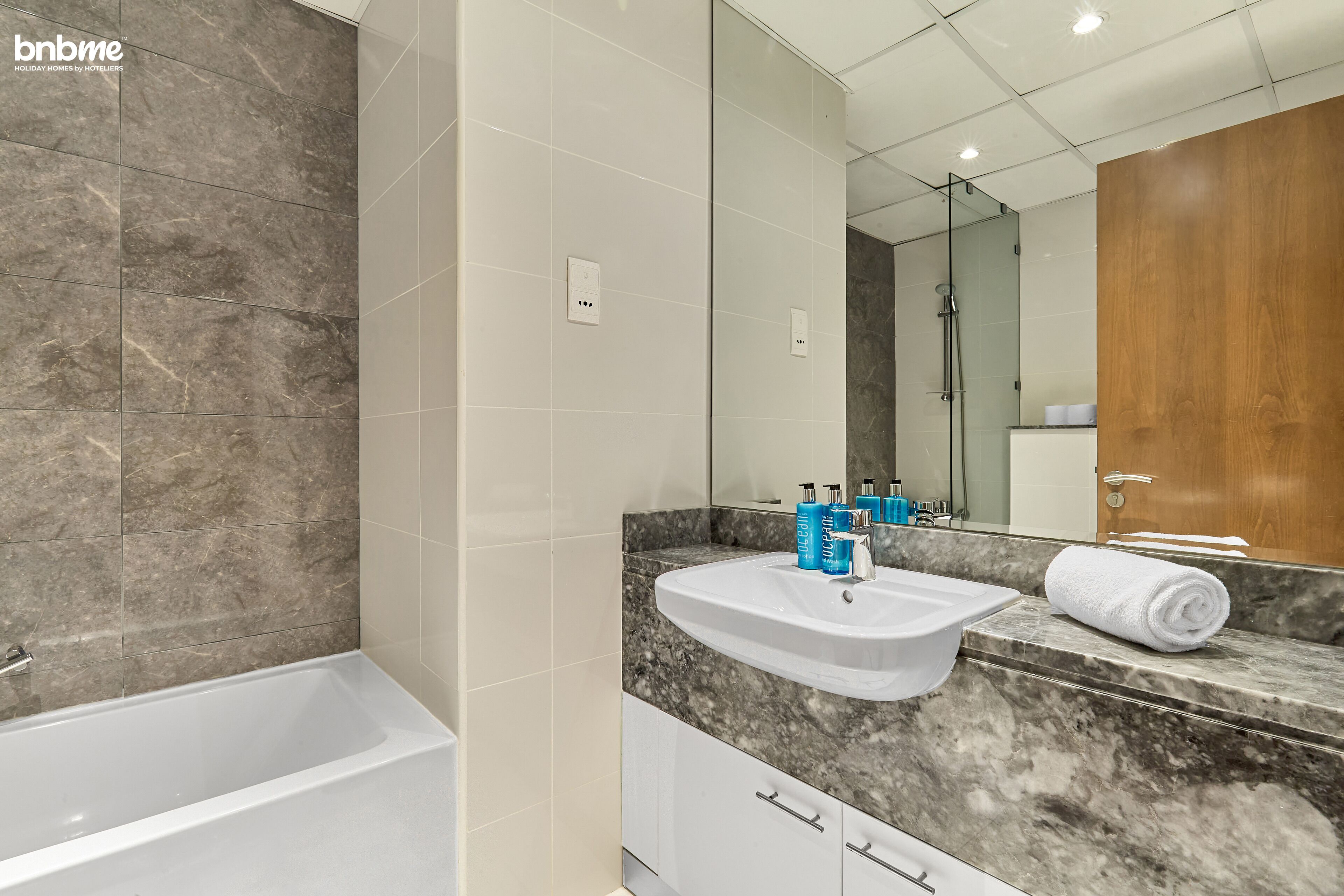A modern bathroom with a bathtub, a sink with toiletries, and a large mirror.
