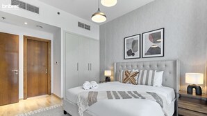 A modern bedroom with a large bed, two bedside tables with lamps, a headboard with decorative pillows, and a wardrobe.