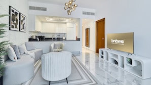 A modern living room with a sofa, a round table, a TV, and a kitchen in the background.