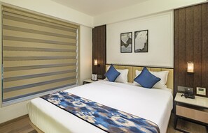 A hotel room with a large bed, a bedside table, a nightstand, and a window with blinds. - Hotel Eden Serenity - Mumbai (Mumbai)