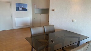 A dining area with a glass table and leather chairs, a white radiator, a picture of a sailboat, and a white cabinet with a shelf. - Apartment in Nieuwpoort near Sandy Beaches (Nieuwpoort)