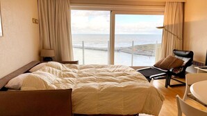 Ein Hotelzimmer mit einem großen Bett, einem Sessel, einem Tisch und Blick auf den Ozean.