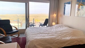 Ein Hotelzimmer mit einem großen Bett, einem Sessel, einem kleinen Tisch und Blick auf die Landschaft durch eine Schiebetür.