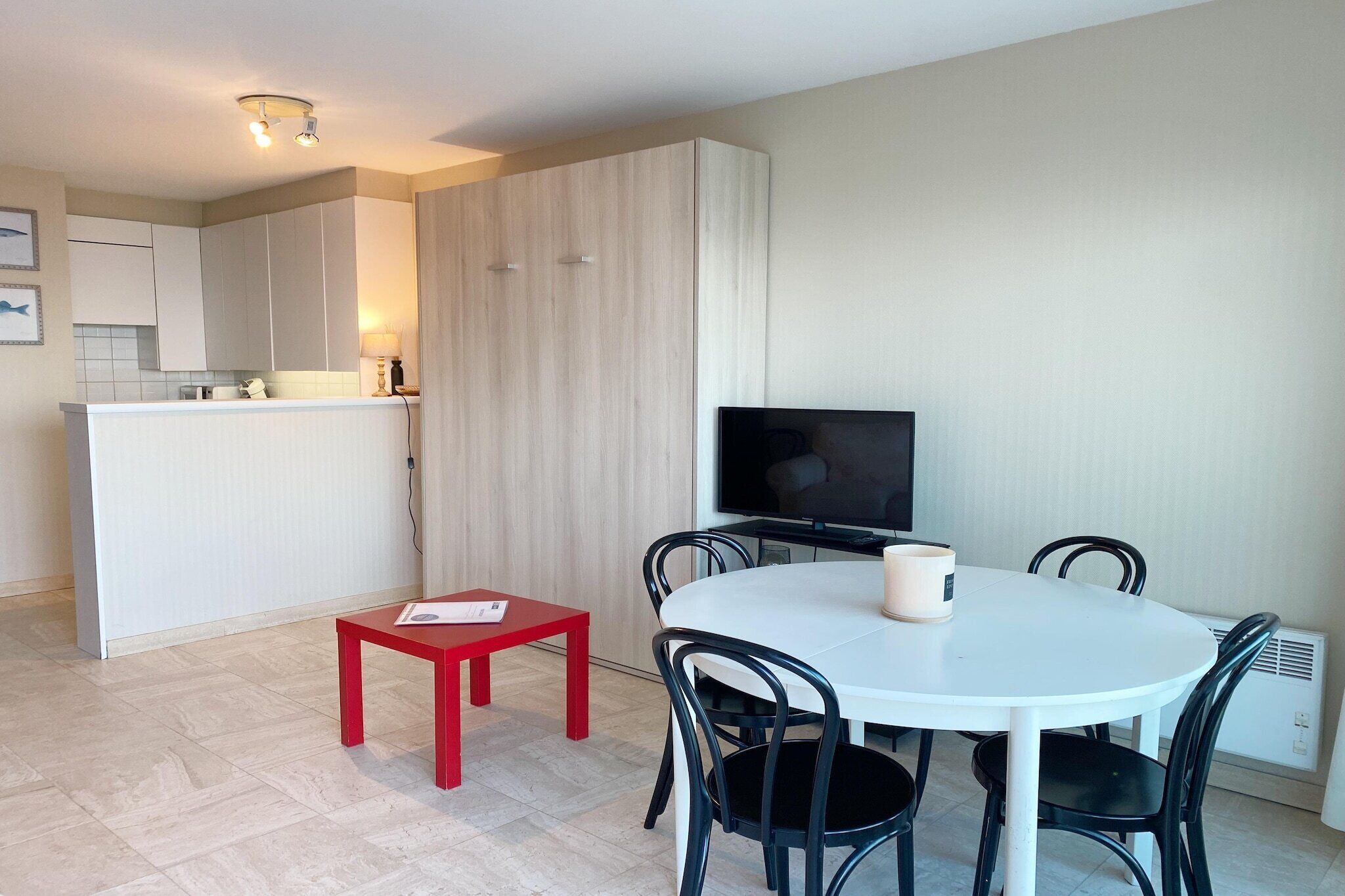 Une cuisine moderne avec des meubles blancs, un coin repas comprenant une table blanche et des chaises noires, et un téléviseur à écran plat posé sur un meuble.