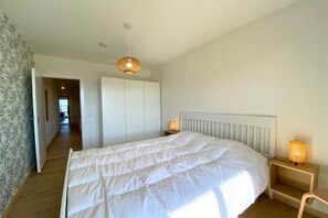 Une chambre à coucher avec un grand lit, une table de chevet avec une lampe, une armoire et une porte donnant sur une autre pièce.