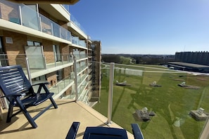 A balcony with a chair, a glass railing, and a view of a green lawn with satellite dishes.