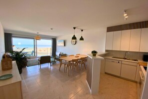 A modern kitchen with a dining area, a view of the beach, and a large window.
