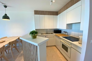 A modern kitchen with white cabinets, a wooden dining table, and a black stove.
