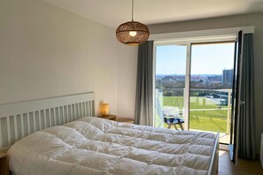 A bedroom with a large bed, a bedside lamp, a view of a green landscape through a sliding door, and a hanging light fixture.