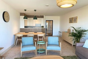 A modern living room with a dining area, a kitchen in the background, and a large potted plant.