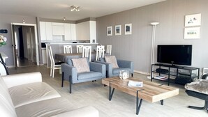 A modern living room with a sofa, two armchairs, a coffee table, and a TV. - Apartment in Nieuwpoort by Scenic Beaches (Nieuwpoort)