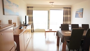A modern kitchen with a dining area, a television, and a balcony with curtains.