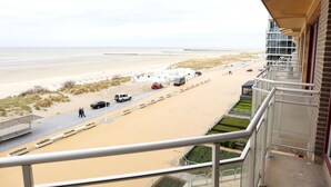 A beach view from a balcony with a sandy beach, a road, and a few vehicles.