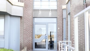 A building entrance with a glass door, brick walls, and a metal staircase.