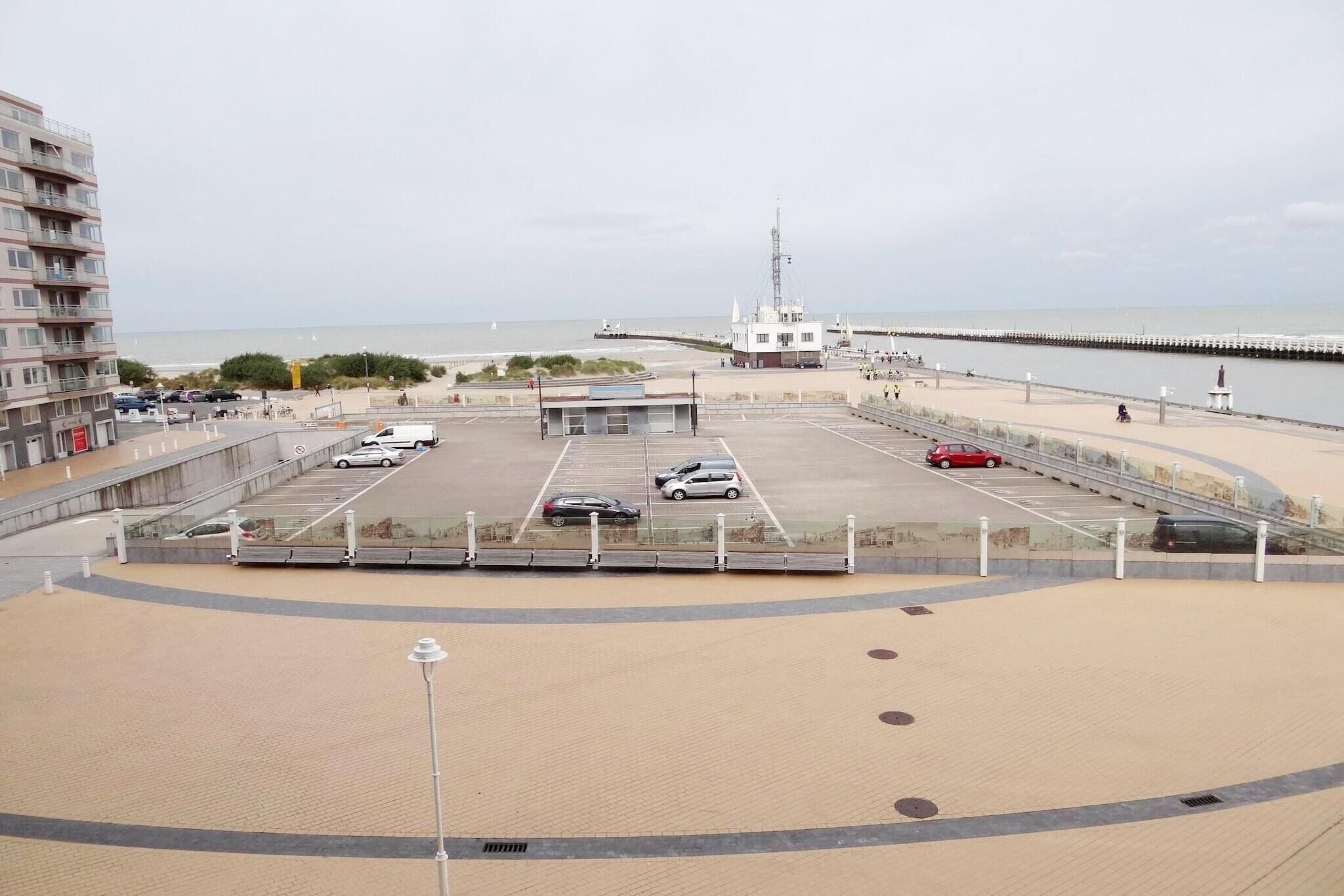 A parking lot with several cars, a building with a flagpole, and a pier extending into the water.