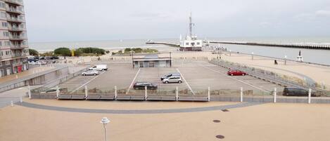 A parking lot with several cars, a building with a flagpole, and a pier extending into the water.