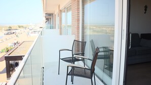 Un balcon avec deux chaises, une table en verre et une vue sur la plage et le paysage urbain.