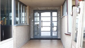 Um corredor estreito com uma porta de vidro que dá para um quarto. O corredor tem piso de azulejos e paredes de tijolo.