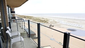 Uma varanda com vista para a praia, cadeiras brancas e um espaço de estar circular.