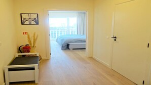 A narrow hallway leading to a bedroom with a bed and a view of a balcony. - Apartment in Nieuwpoort near the Beach (Nieuwpoort)