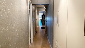 Un pasillo estrecho con suelo de madera y paredes texturizadas, que lleva a una habitación con una puerta y un escalón pequeño.