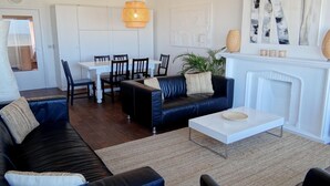 A modern living room with a black leather sofa, white coffee table, and a dining area with a white table and chairs. - Nieuwpoort Central Retreat (Nieuwpoort)