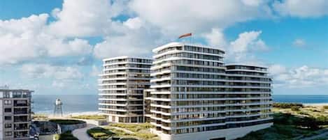 A modern hotel with multiple floors, a flag on top, and a view of the sea.