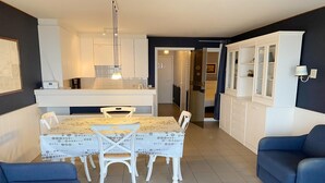 A modern kitchen with white cabinets, a dining table with chairs, and a blue sofa. - Apartment in Nieuwpoort with Ocean Views (Nieuwpoort)