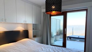 A bedroom with a large bed, white walls, and a sliding glass door leading to a balcony. - Attic Apartment in Nieuwpoort by the Beach (Nieuwpoort)