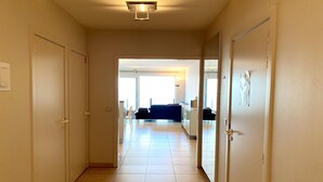 Un couloir carrelé mène à un salon comprenant un canapé et une table basse.