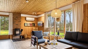 A cozy cabin interior with a fireplace, wooden furniture, and large windows offering a view of the outdoors. - "Sofja" - 175m to the fjord by Interhome (Hadsund)