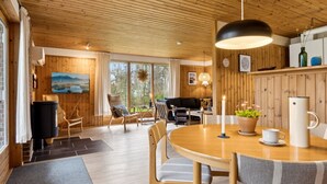 A cozy cabin interior with a wooden ceiling, a dining area with a round table, and a seating area with chairs. - "Sofja" - 175m to the fjord by Interhome (Hadsund)
