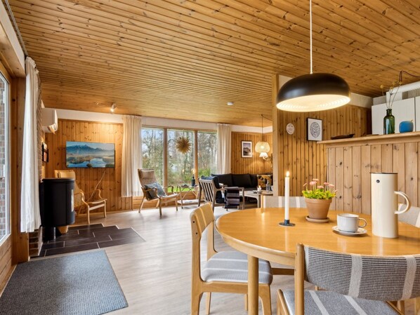 Ein gemütliches Blockhaushaus-Interieur mit Holzbalkendecke, einem Essbereich mit rundem Tisch und einer Sitzecke mit Stühlen.