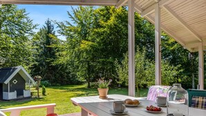 A covered patio with a white table set for a meal, surrounded by lush greenery and a small garden. - "Sofja" - 175m to the fjord by Interhome (Hadsund)