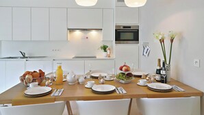 A modern kitchen with white cabinets, a wooden dining table set with plates, cups, and a fruit bowl. - Apartment Nieuwpoort near Beach and Marina (Nieuwpoort)