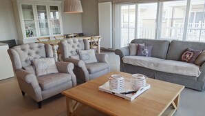 A living room with two grey armchairs, a grey sofa, a wooden coffee table with a tray of items, and a dining area with a table and chairs. - Apartment in Nieuwpoort near the Beach (Nieuwpoort)