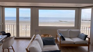 A spacious living area with a large sliding glass door leading to a balcony overlooking a beach. - Apartment Nieuwpoort near Sandy Beaches (Nieuwpoort)