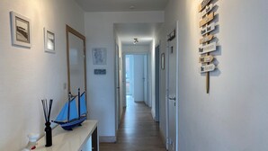 A hallway with wooden flooring, a white console table with a decorative sailboat, a black bottle, and a wall-mounted sign with motivational phrases. - Apartment Nieuwpoort near Sandy Beaches (Nieuwpoort)