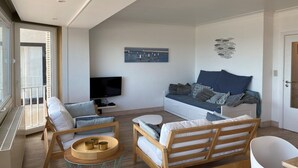 A modern living room with a sofa, chairs, a TV, and a balcony. - Apartment Nieuwpoort near Sandy Beaches (Nieuwpoort)