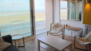 Une chambre moderne dotée d’une grande porte-fenêtre coulissante donnant sur la plage, d’une petite table ronde, d’un canapé et d’un banc en bois.