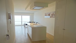 A modern kitchen with a central island, a dining area with chairs, and a large window providing natural light. - Apartment in Nieuwpoort by the North Sea (Nieuwpoort)