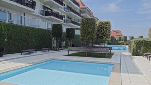 Een zwembadgedeelte met een betegeld terras, bankjes en keurig gesnoeide hagen.