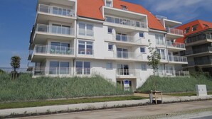 Een meerlaags woongebouw met balkons, een rood dak en een kleine boom ervoor.