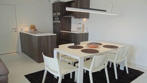 Een moderne keuken met een centraal eiland, witte kastjes en een eethoek met een witte tafel en stoelen.