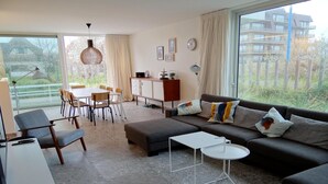 A modern living room with a sofa, coffee table, and dining area. - Apartment in Nieuwpoort by Beach (Koksijde)