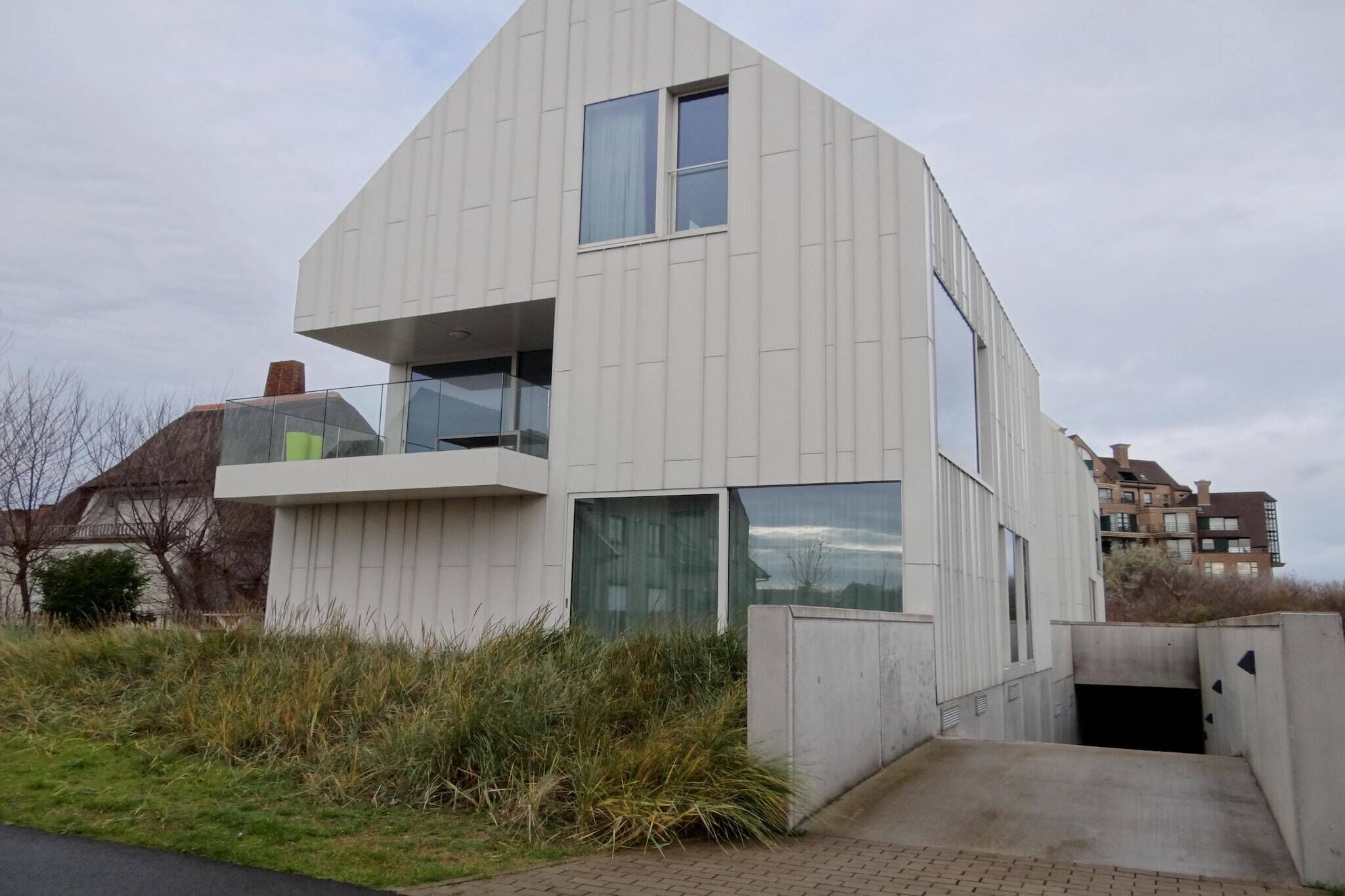 A modern two-story building with a flat roof, large windows, and a visible balcony.