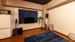 Un espacio habitable pequeño con kitchenette, televisor, alfombra azul y un letrero motivacional en la pared.